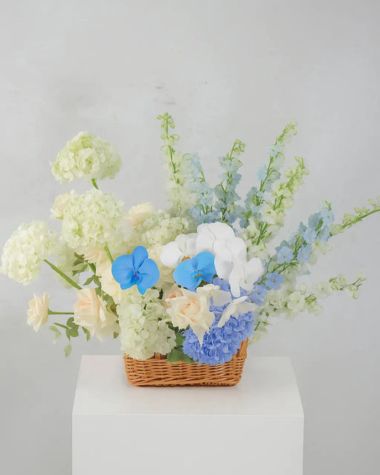 Luxury flower arrangement in Dubai featuring a rare sky-blue orchid, white roses, and hydrangeas in a wicker basket