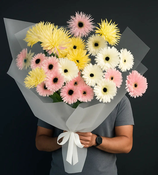 Golden Dawn Bouquet with yellow, pink, and white gerbera daisies wrapped in white paper against a dark background.