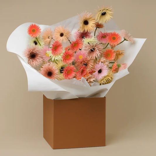 Pastel Breeze bouquet with bright gerbera daisies in pink, orange, and yellow, arranged in a white paper wrap and kraft box – same-day flower delivery in Dubai.
